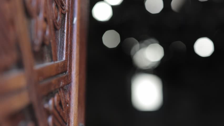 A wooden door with beautiful patterns in the semi-darkness of a stone church. Beautiful chandeliers are visible in the background.