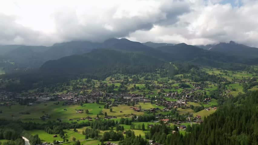 Aerial 4K timelapse of fast moving clouds rolling over the Grindelwald valley in the Swiss Alps with shifting light on mountains and fields.