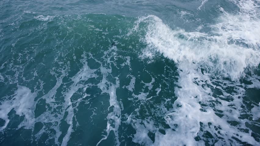 Dynamic turquoise sea waves surge into jagged rocks beneath a heavy gray sky, exploding into white spray and droplets, perfect as dramatic coastal stock footage. - Powered by Shutterstock - Get 15% off with code: PIKWIZARD15