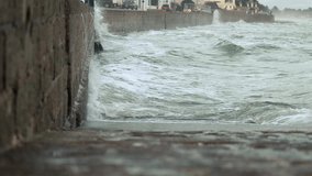 Powerful turquoise storm waves crash against a coastal breakwater, sending dramatic spray over parked cars under dark, menacing clouds. - Powered by Shutterstock - Get 15% off with code: PIKWIZARD15
