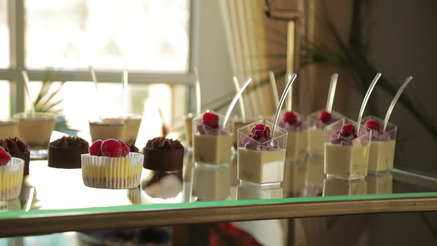 Beautiful white individual desserts in transparent cups, nicely arranged on a table, with a beige filling and decorated with raspberries.