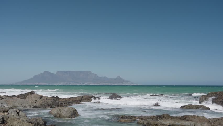 Waves break onto Blouberg shore, with stunning views of Table Mountain, Devil’s Peak, and Signal Hill in Cape Town, Western Cape, South Africa. Perfect coastal nature footage in 4K 30fps.