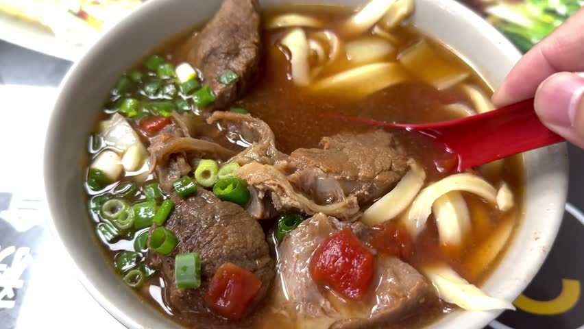 Classic Beef Cheek Noodles with chilli sauce, spring onion,tomato, wooden spoon, and chopsticks served in dish isolated on mat side view of taiwanese food