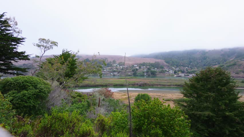 A misty valley landscape with a winding river and lush green trees, surrounded by distant hills and soft morning fog under cloudy skies
