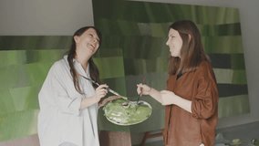 Two women joyfully create abstract art together in a bright studio filled with colorful paintings - Powered by Shutterstock - Get 15% off with code: PIKWIZARD15