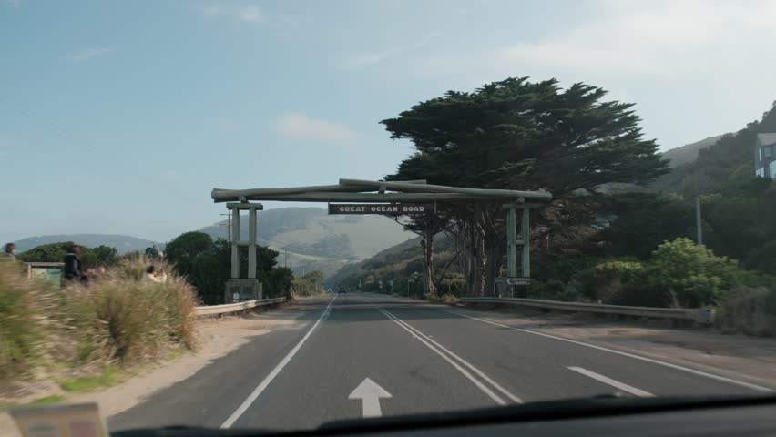 Driving POV passing under the iconic timber Great Ocean Road Memorial Arch in Victoria, Australia. Start of the famous scenic coastal drive on a sunny day.