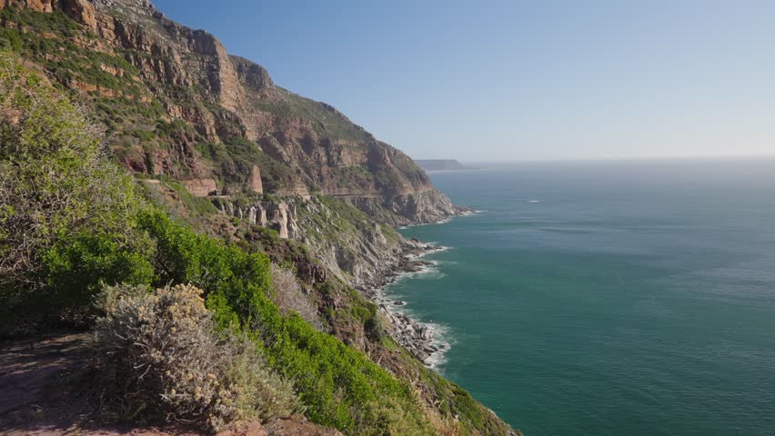 Coastal view along Chapman’s Peak Drive at Hout Bay, Cape Town, Western Cape; rugged cliffs, blue ocean, winding road, iconic South African landscape under clear sky. 30fps footage captured in 4k 60p.