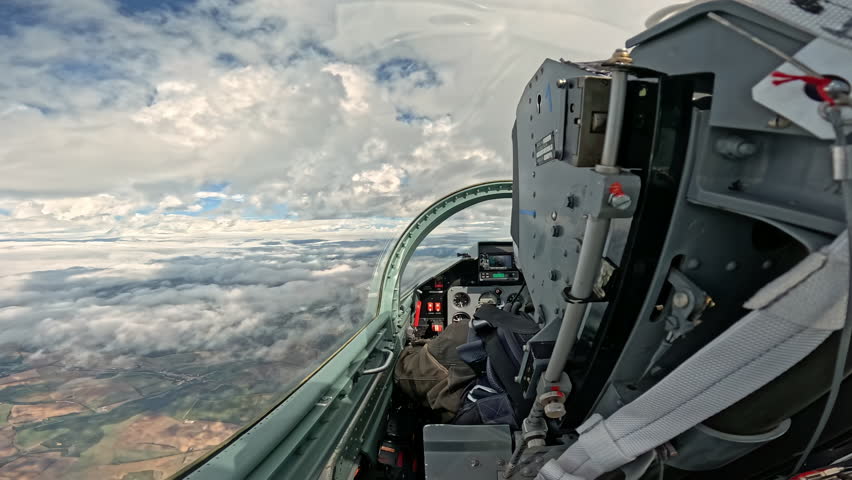 View from the fighter jet cockpit on the white clouds and landscape below, interior of the military aircraft flying high in the sky during the day mission