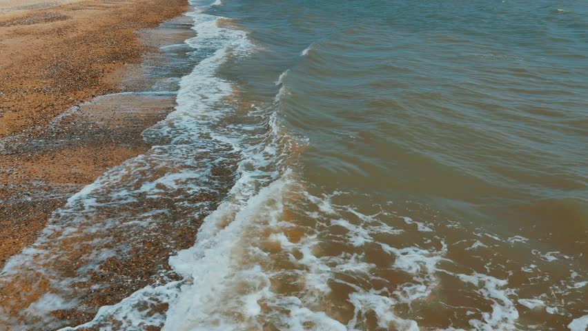 Gentle waves roll onto a sandy shoreline, blending blue water with foamy white surf under daylight