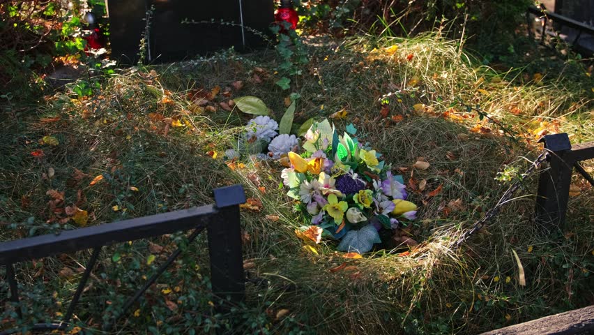 Neglected Grave Tombstone with Old Fake Plastic Flowers Decoration Overgrown with Grass