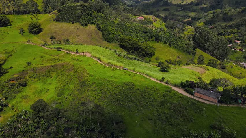 A drone view of rolling green hills and a winding rural path near Jardin, surrounded by dense vegetation and farmland across the Andean countryside