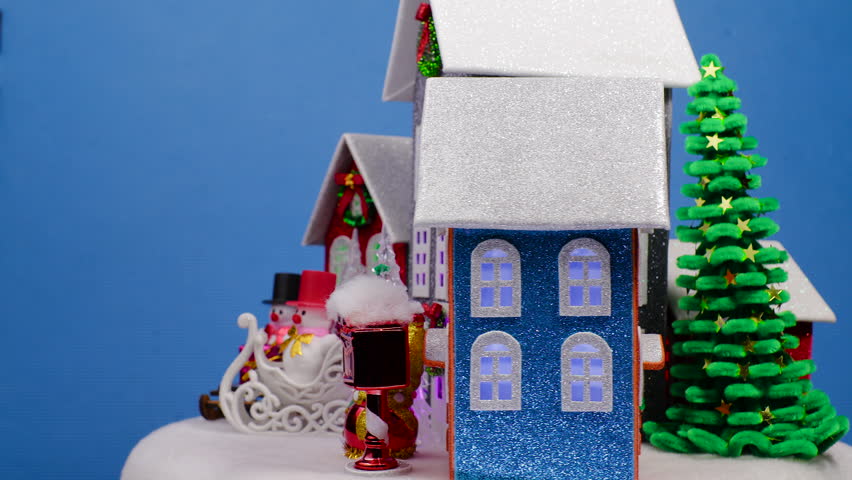Multicolored houses with flashing lights in the windows, surrounded by small Christmas trees and snowmen on sleds and without, spinning against a blue background