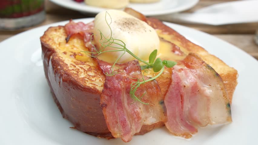 A close-up view of a poached egg resting on toasted bread with crispy bacon. Ideal for themes of brunch, gourmet food, cooking, and cafe-style meals.