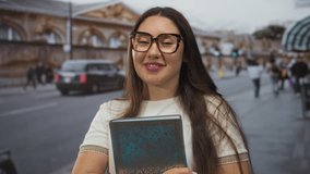 Woman holds patterned book close to body on busy city street with passing cars and blurred pedestrians; inspiration. - Powered by Shutterstock - Get 15% off with code: PIKWIZARD15