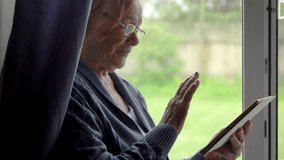 Elder woman engaging with tablet. Elderly lady enjoying online communication in cozy setting. Old female navigating touch screen device by window in serene environment. Granny discussion with family - Powered by Shutterstock - Get 15% off with code: PIKWIZARD15
