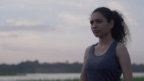 A Smiling South Asian woman with curly hair performing prayer hands pose (Anjali Mudra) during outdoor yoga by a lake at sunset - Powered by Shutterstock - Get 15% off with code: PIKWIZARD15