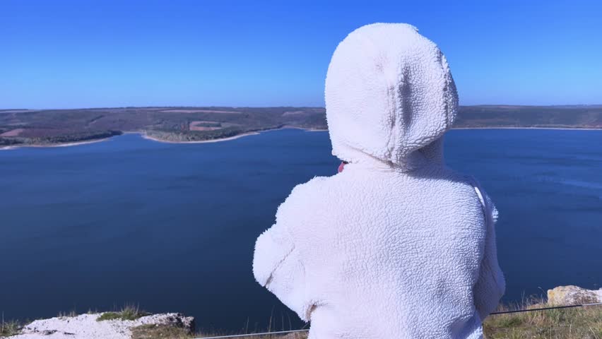 A beautiful young girl looks into the distance enjoying the gorgeous view of a mountain lake.