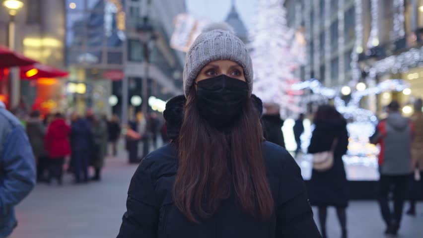 Woman in medical mask waiting on city street in Winter at Christmas