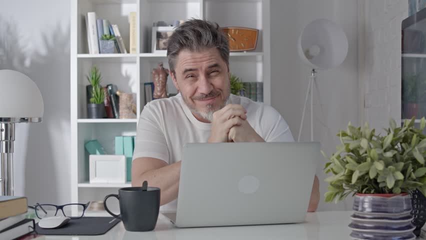 Portrait of middle aged man sitting at desk in morning at home. ,Drinking coffee reading news on laptop. Businessman staying home working in home office with computer, smilin g.