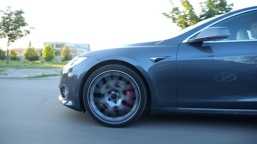 Handsome businessman in shirt driving a modern electric car at urban road. Male successful entrepreneur riding on electrical vehicle at city. Young man commuting to work at sunny day. Slow motion