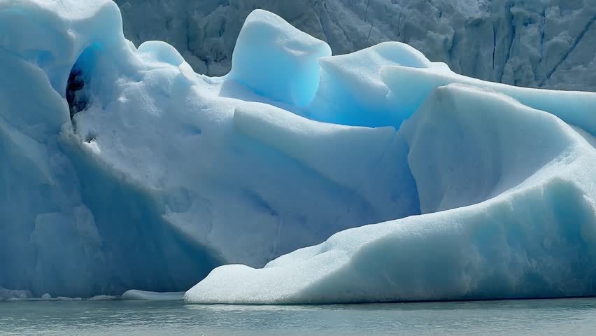 A massive blue iceberg drifts across Lake Argentino in Patagonia, Argentina, near the Perito Moreno Glacier, showing calm water and ice texture.