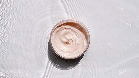 A jar of white cream on a water surface. Splash of water, sunlight and shadows. Layout for advertising goods, cosmetic products. Medical skin care, body care. - Powered by Shutterstock - Get 15% off with code: PIKWIZARD15