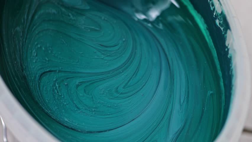 Vibrant teal paint is being stirred in a container, revealing its smooth texture and rich color, with a gradual zoom in capturing the mixing action