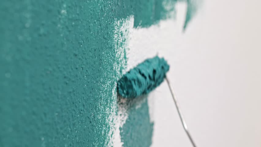 Male painter applies blue paint to wall with roller, camera captures action progression