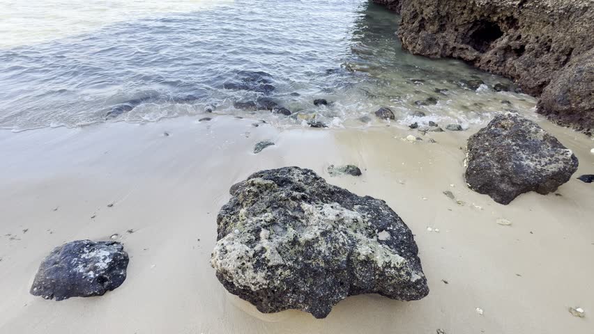 a gorgeous summer landscape at the beach with large rocks in silky brown sand surrounded by blue ocean water and waves rolling into the beach with powerful clouds at sunset at Leadbetter Beach 