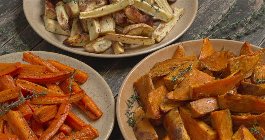 Baked vegetables: parsnip, carrot, and sweet potatoes. Roasted root vegetables with honey and thyme on three plates. Table spin.