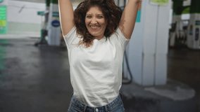 Woman in white t shirt raising arms and smiling with clenched fists at petrol station forecourt by fuel pumps and columns; joy victory celebration. - Powered by Shutterstock - Get 15% off with code: PIKWIZARD15