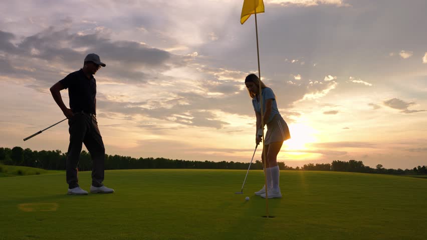 Asian man and woman golfers swing clubs together on scenic golf course. Attractive people enjoy fun game outdoor recreation and light exercise while practicing under the guidance of trainer in course.