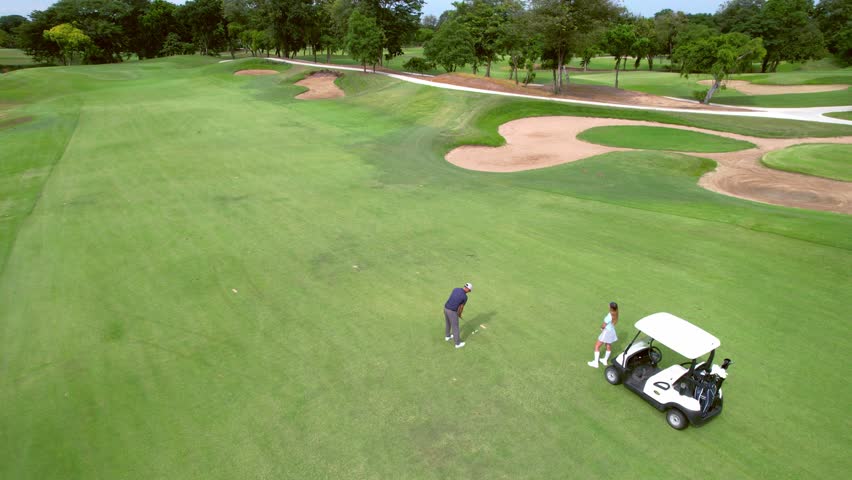 Drone view of young golfers swing clubs together on a scenic golf course. Attractive man and woman enjoy outdoor recreation with light exercise and sport lifestyle while playing golf at course ground.