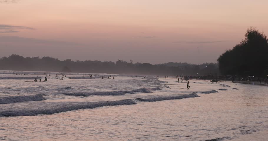 Public town beach in Weligama at sunset with surfers, Sri Lanka