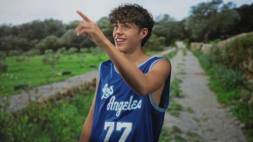 Teen boy in a blue los angeles basketball jersey reaching up with hand on a forest path; aspiration youthful energy.
