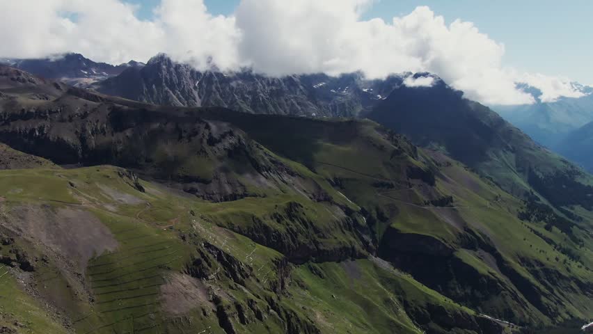 A panoramic drone view of mountain slopes with terraces, showing layered terrain, cultivated land, and dramatic high-altitude scenery with natural textures and patterns.

