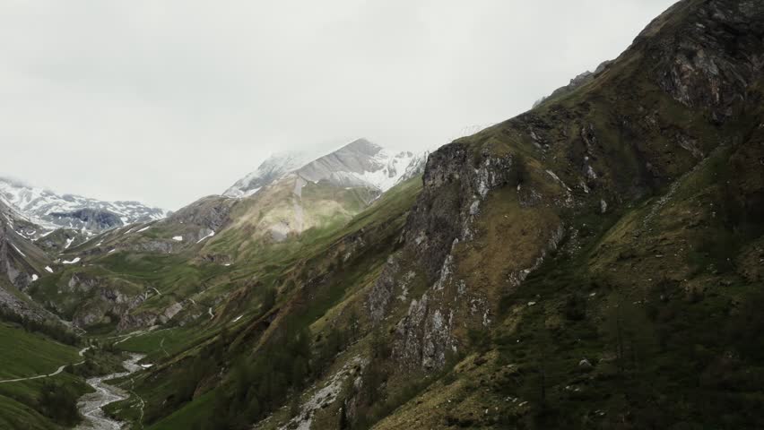 Panoramic view of a high alpine valley with rocky peaks, showcasing dramatic mountains, green slopes, and scenic natural beauty.