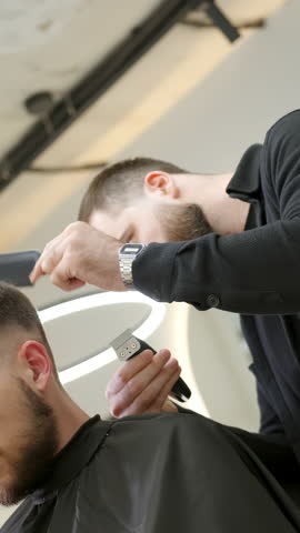 Professional barber giving haircut to male client. Clip
