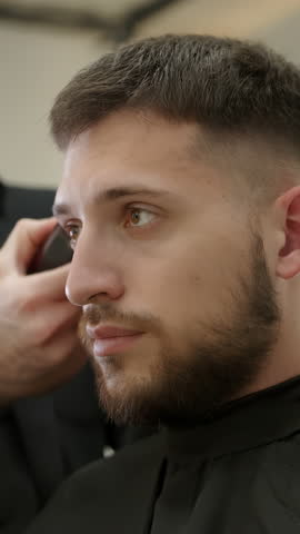 Professional barber giving haircut to client with electric trimmer. Clip