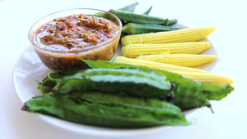 Boiled winged beans, baby corn, and okra are served on a plate with a spicy Thai-style chili paste.