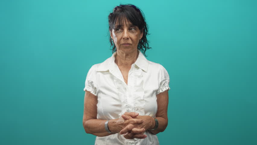 Woman cupping right hand to ear in studio, mouth open in a surprised listening pose, wearing white blouse and silver cuff bracelet; surprise listening.