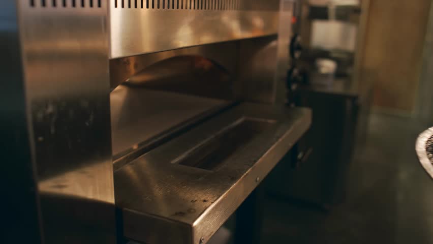 Close-up of a chef putting raw pizza into an oven with a metal peel in a dark kitchen, highlighting cooking, baking, and culinary action.