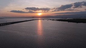 Cinematic drone view of the Davao Coastal Road causeway during a dramatic golden sunset. A modern highway curving along the shoreline with a bright sun reflection on the calm ocean water. - Powered by Shutterstock - Get 15% off with code: PIKWIZARD15