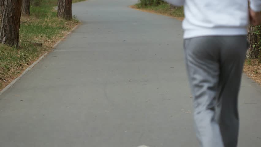 Tilt-up rear view of an unrecognizable elderly man with grey hair running along a path, highlighting fitness and outdoor activity.
