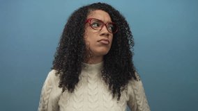Woman with curly hair wearing red glasses and white cable knit sweater raises hands palms up in studio; confusion. - Powered by Shutterstock - Get 15% off with code: PIKWIZARD15