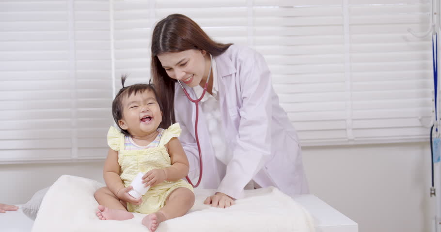 Asian pediatrician listening to toddler chest with stethoscope in slowmotion scene, smiling gently during medical examination, expressing care, trust, and compassion, concept of child health checkup 