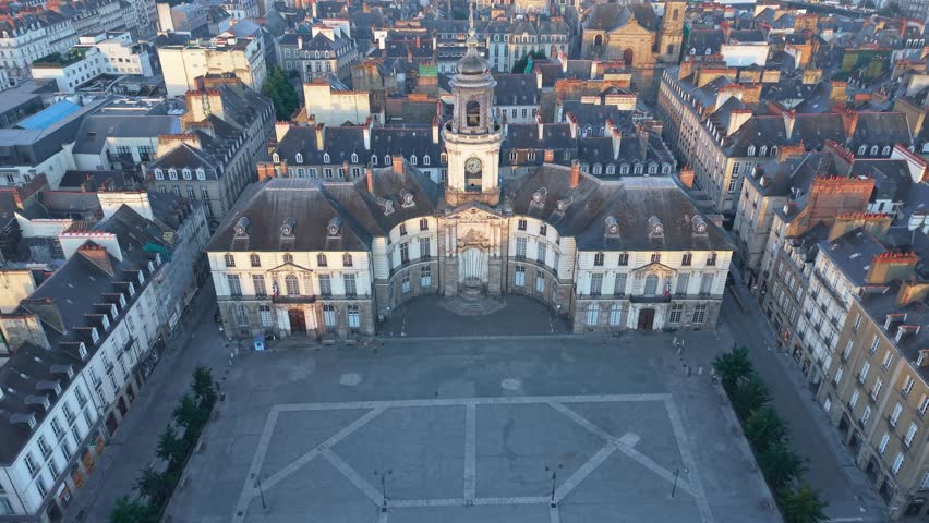 Drone push in over historic Hôtel de Ville de Rennes, a grand U-shaped classical building with its iconic clock tower and ornate symmetrical wings within Place de la Mairie in the heart of the city.