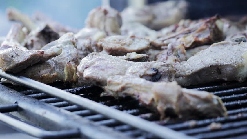 Roasting pork ribs on a grill grate in a barbecue oven, slow motion, close-up