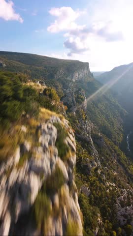 Extreme FPV Drone Dive Down a Steep Mountain Cliff into a Rapid Turquoise River Canyon with Sun Flare
