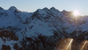 Cinematic aerial view of sunrise over a snowy mountain ridge with bright sun flare. Inspiring morning alpine landscape backlight view. - Powered by Shutterstock - Get 15% off with code: PIKWIZARD15